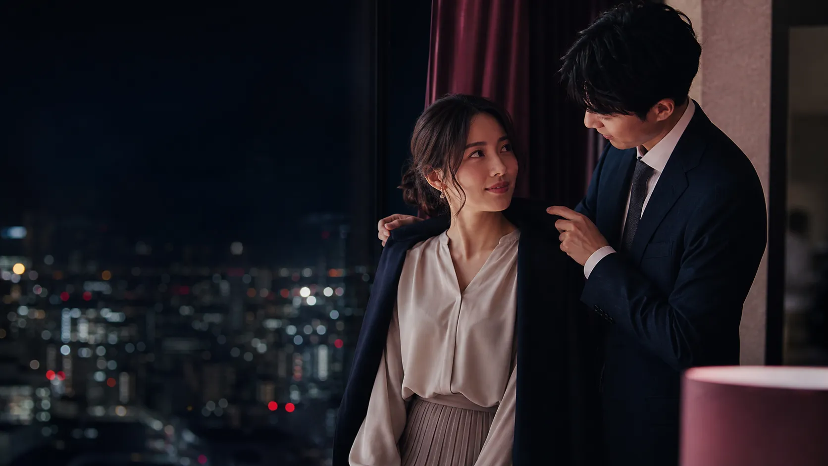 夜景の前でコートを掛け合う成人男女